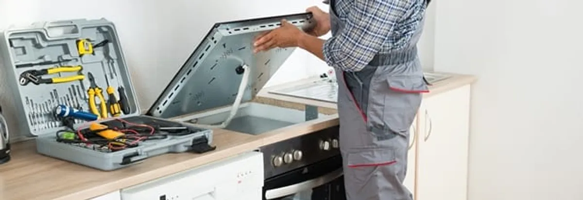 Cooktop repair technician lifting a built-in stovetop for service in Cambridge, MA
