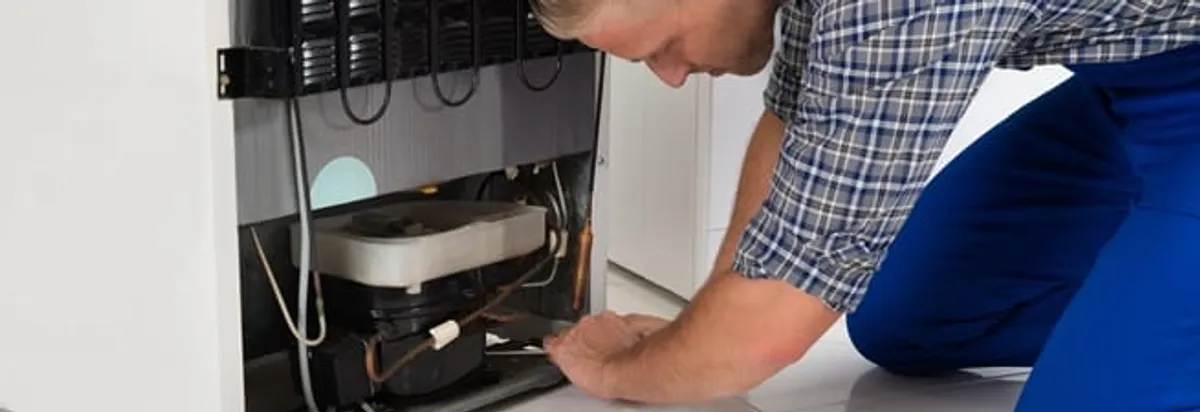 Refrigerator repair technician servicing the compressor and condenser area in Cambridge, MA